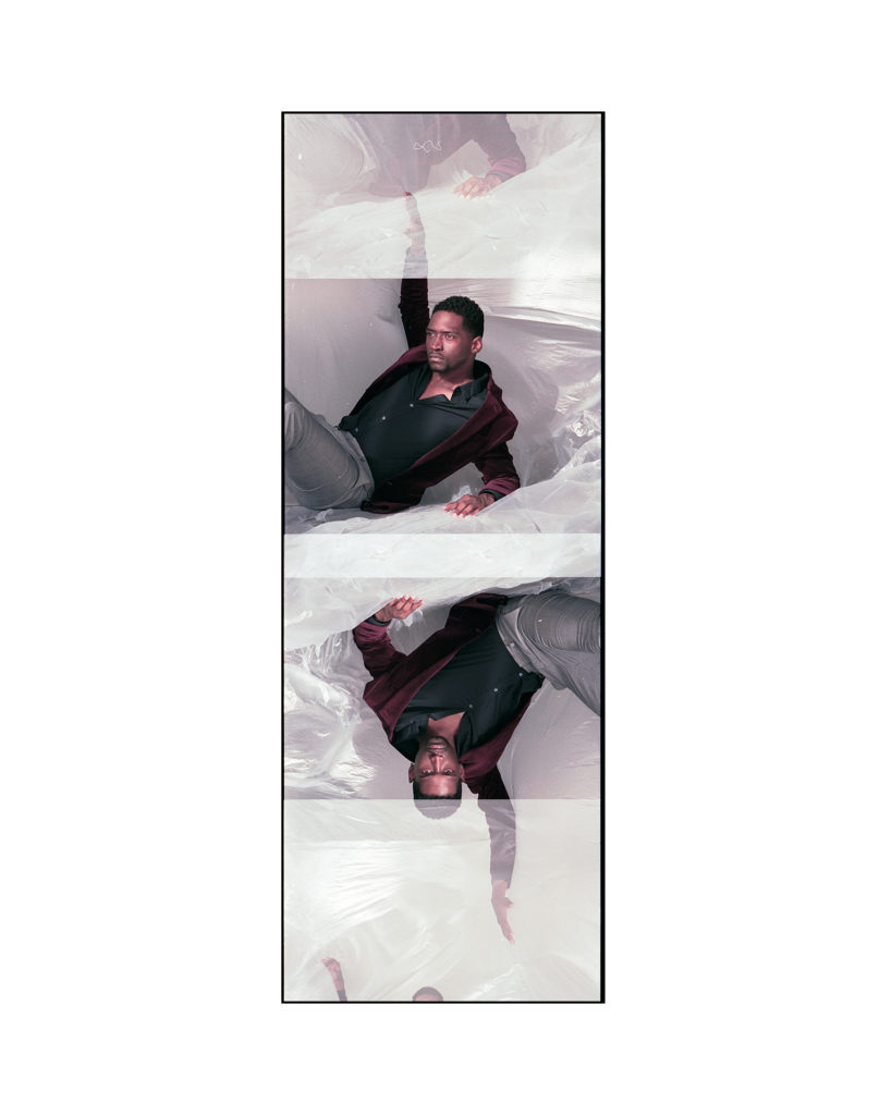 A double exposure of a Black male model is seen inverted, where he's raising his right arm above his head and turned toward the light at a profile view. He is leaning back, seated, on top of a sheet of moving plastic.